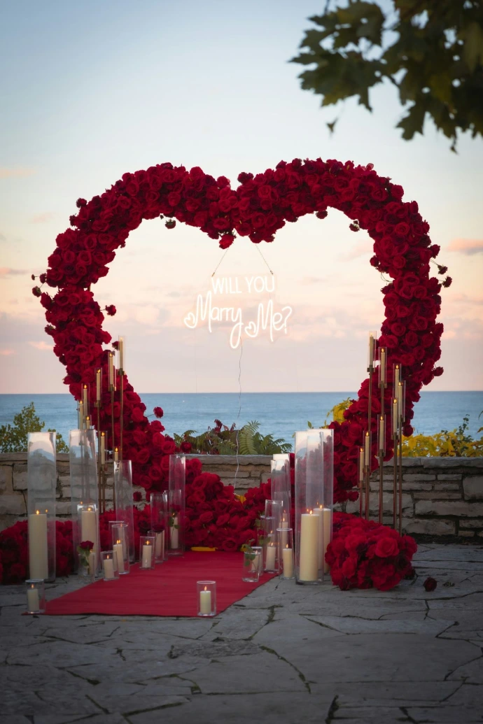 Heart-shaped floral arch with proposal message by the ocean.